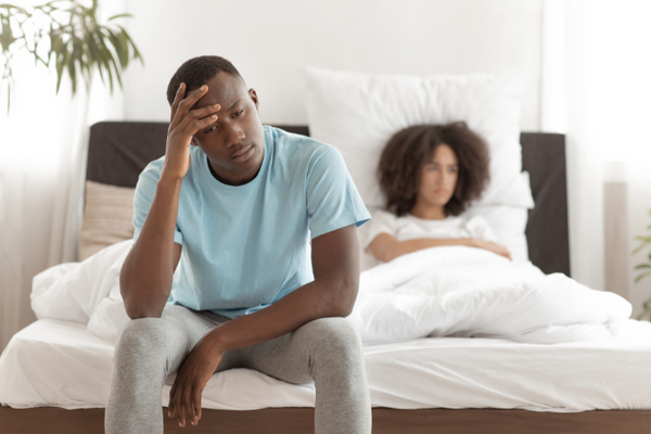 Man in distress over erectile dysfunction sitting on bed - natural ED solutions concept.